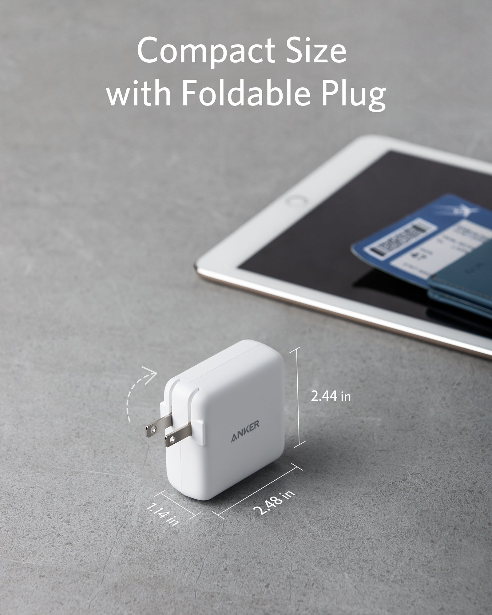 Compact white power adapter with foldable plug on a gray surface, next to a tablet.